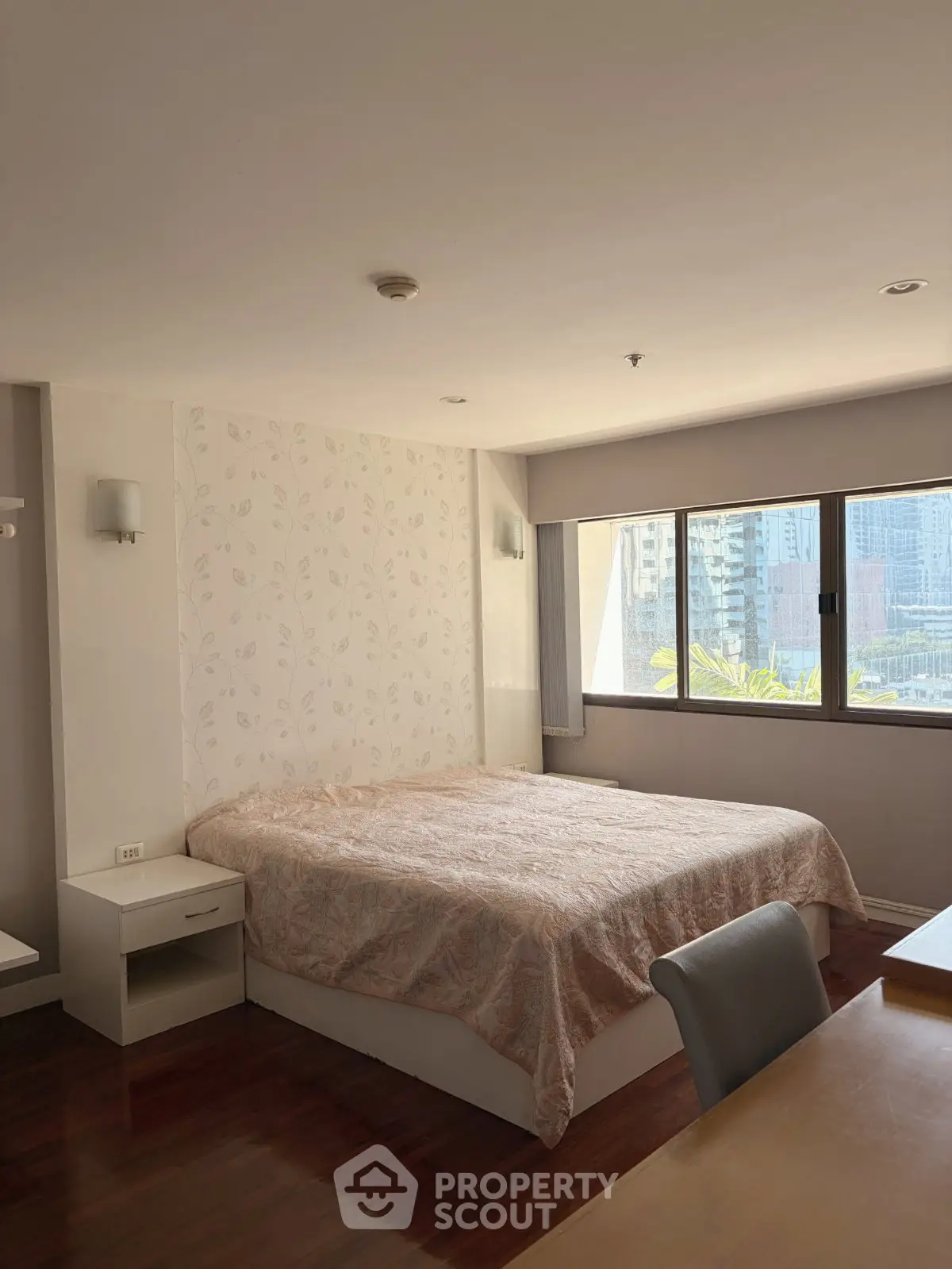 Spacious bedroom with large window offering city views, featuring elegant decor and natural light.