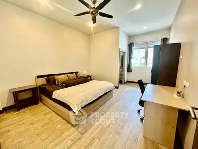 Spacious bedroom with modern furnishings and natural light, featuring a comfortable bed and work desk.