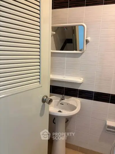 Compact bathroom with pedestal sink and wall-mounted mirror in modern apartment.