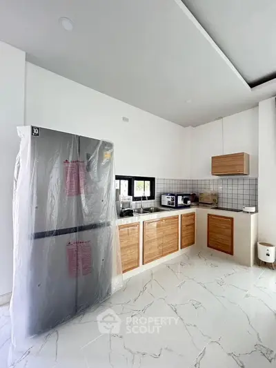 Modern kitchen with new fridge and wooden cabinets in a bright, spacious setting.