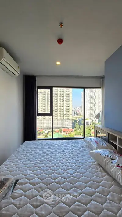 Modern bedroom with large window offering stunning city view in high-rise apartment.