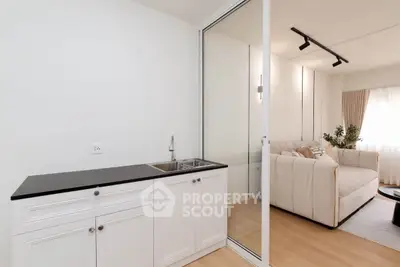 Modern living room with sleek design and compact kitchenette, featuring elegant white cabinetry and cozy seating area.