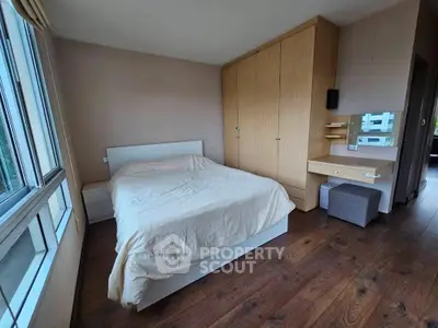 Spacious bedroom with large windows and wooden flooring, featuring a cozy bed and ample storage.