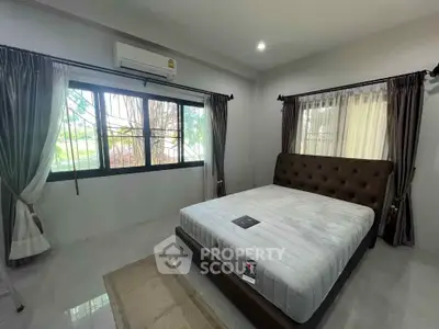 Spacious bedroom with large windows and elegant curtains, featuring a modern bed and air conditioning.
