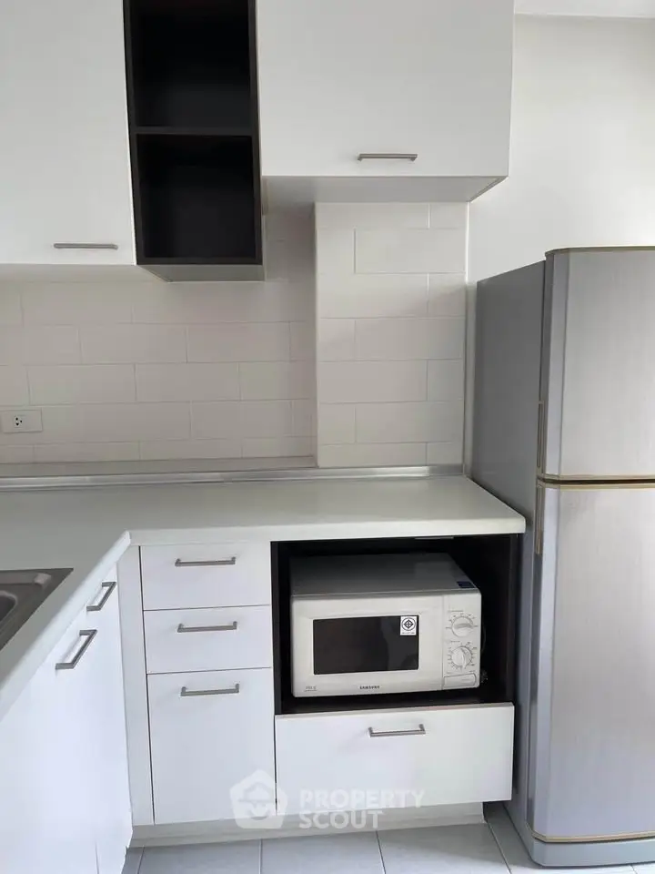 Modern kitchen with sleek white cabinets and built-in microwave, featuring a spacious fridge.