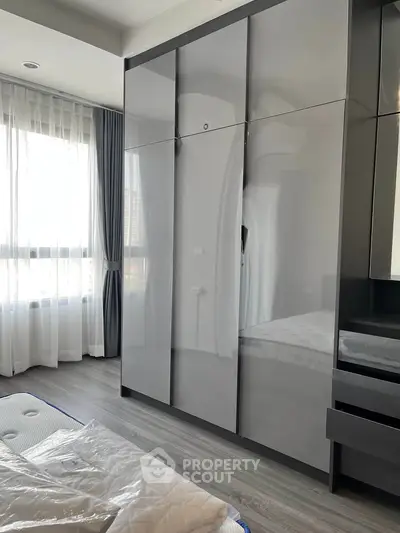 Modern bedroom with sleek wardrobe and large window for natural light.