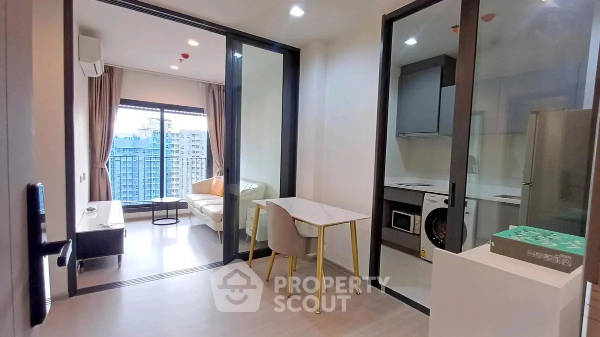 Modern apartment interior with open living room and kitchen, featuring large windows and stylish furniture.