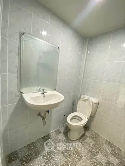 Modern bathroom with tiled walls and floor, featuring a sink and toilet.