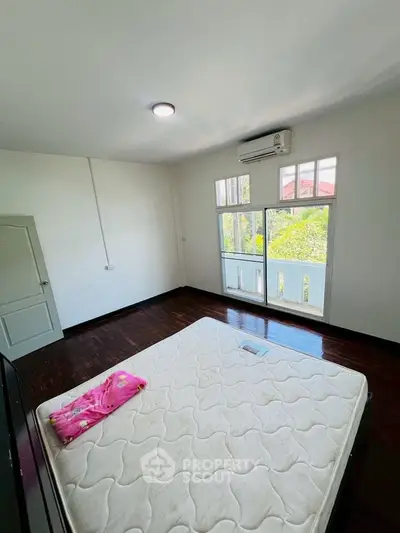 Spacious bedroom with large windows and air conditioning, featuring a comfortable mattress.