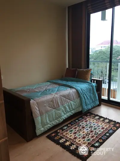 Cozy bedroom with large window offering natural light and a serene view, complemented by a warm wooden bed frame and an elegant patterned area rug.