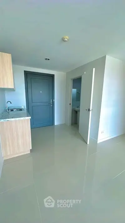 Modern apartment entrance with sleek kitchen and bathroom access, featuring glossy tile flooring.