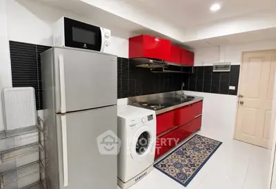 Modern kitchen with red cabinets, stainless steel fridge, and washing machine in sleek apartment.