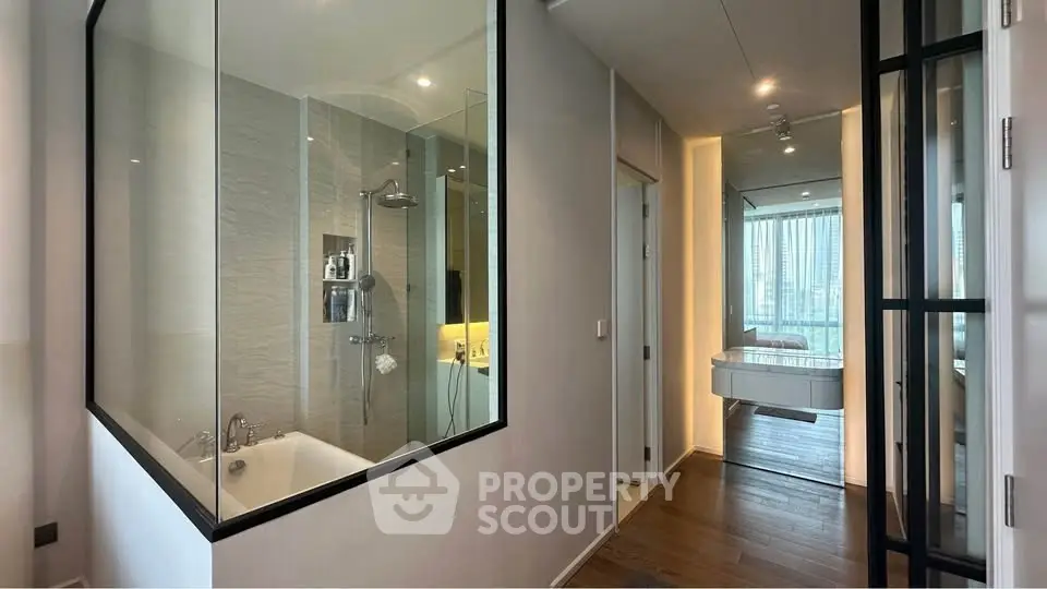 Modern apartment interior with glass-walled bathroom and city view, featuring sleek design and wooden flooring.