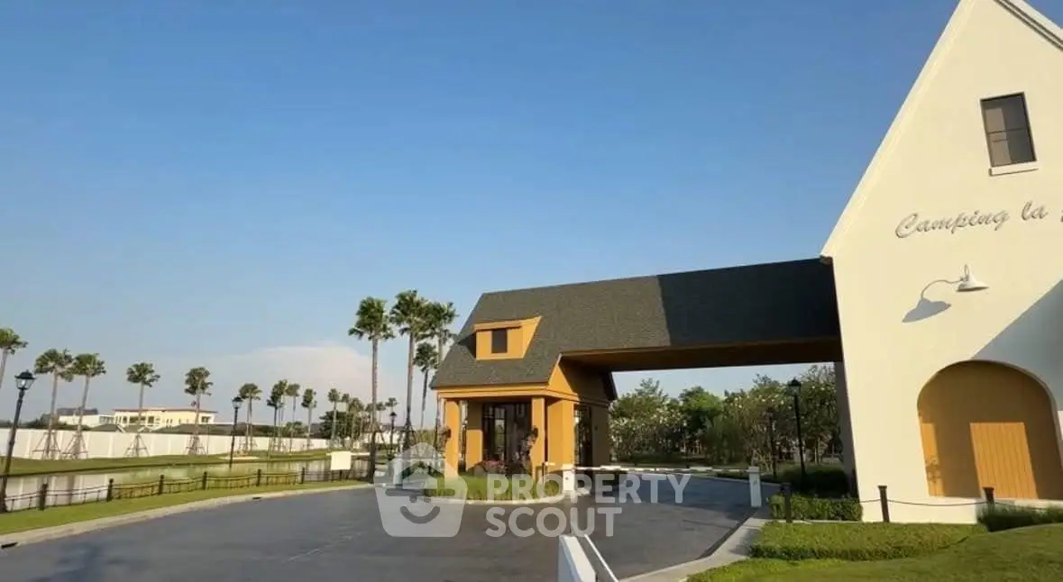 Charming entrance of a modern estate with lush greenery and clear blue skies.
