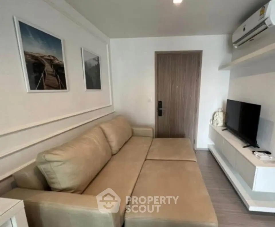 Modern living room with beige sofa, wall-mounted TV, and air conditioning unit.