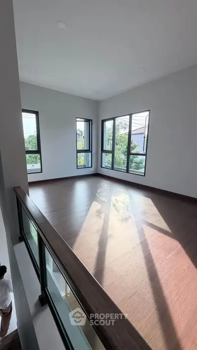 Spacious sunlit room with large windows and wooden flooring, perfect for a modern living space.