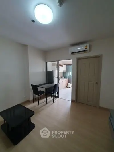 Modern apartment interior with dining area and kitchen, featuring sleek furniture and air conditioning.