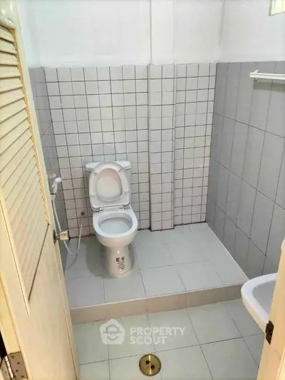 Compact bathroom with tiled walls and floor, featuring a toilet and sink, ideal for efficient space use.