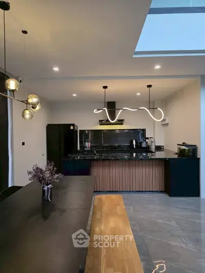 Modern kitchen with sleek black cabinetry and unique lighting fixture, featuring a spacious dining area.