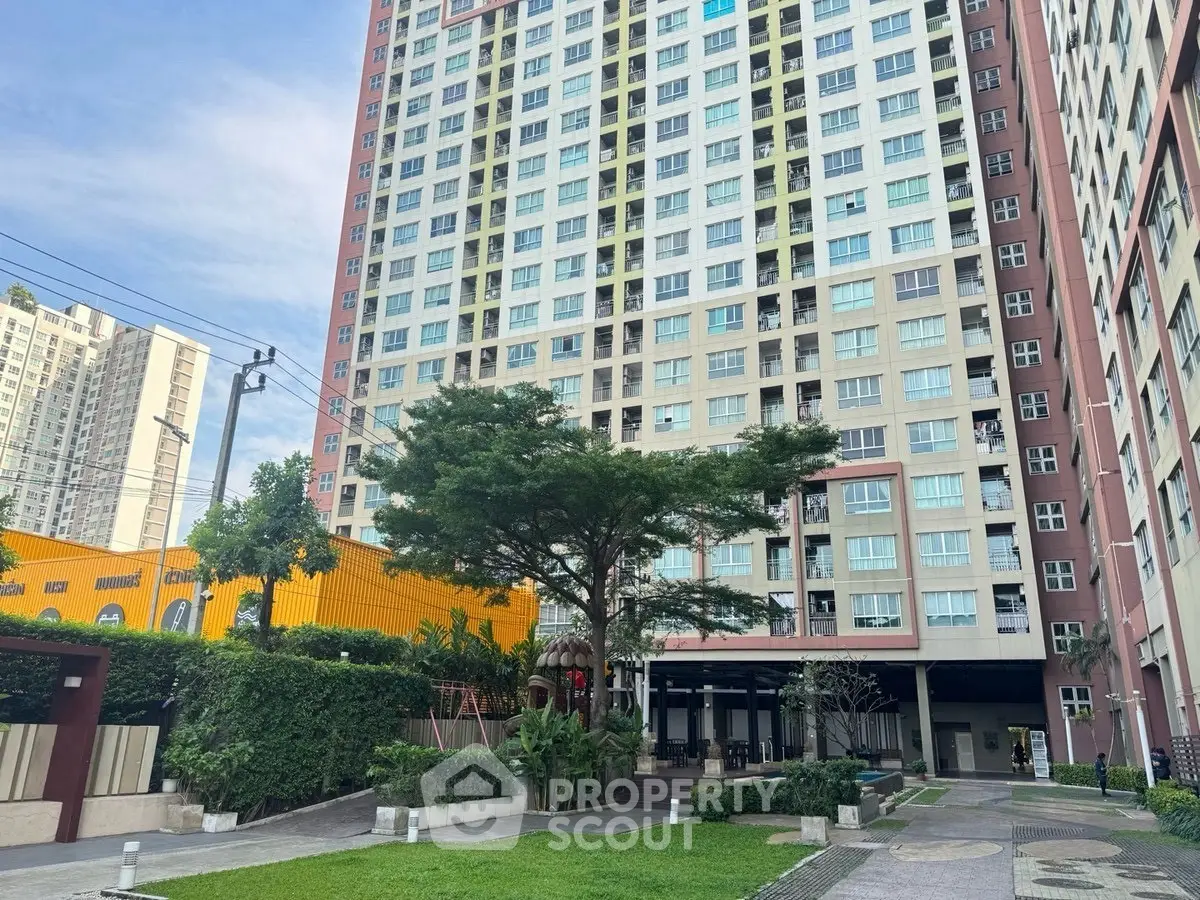 Modern high-rise residential building with lush green landscaping and spacious outdoor area.