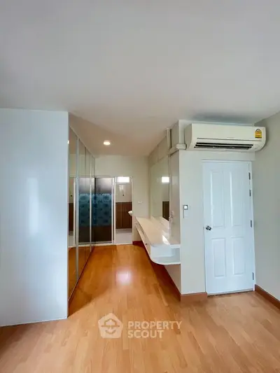 Spacious modern bedroom with wooden flooring and built-in wardrobe, featuring air conditioning for comfort.