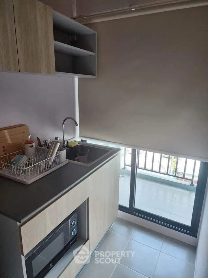 Modern compact kitchen with sleek cabinetry and built-in microwave, featuring a large window for natural light.