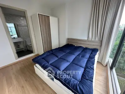 Modern bedroom with large window and blue bedding, featuring a view of greenery.
