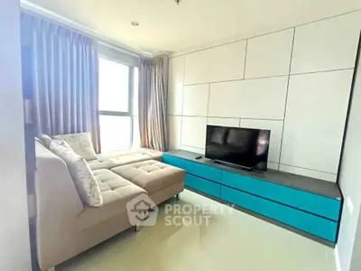 Modern living room with stylish sofa and TV unit, featuring large windows and elegant curtains.