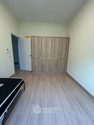 Spacious and well-lit empty room with modern wood-like flooring and a large built-in wardrobe, perfect for customization and personalization.