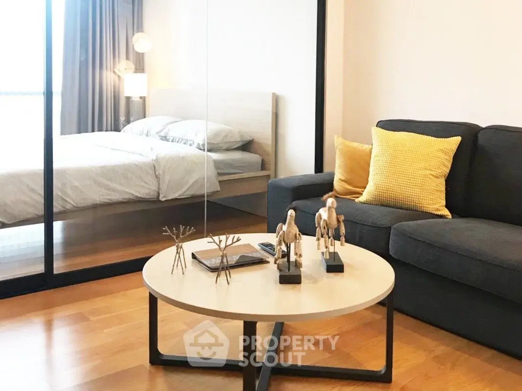 Modern living room with cozy sofa and stylish decor adjacent to a bedroom with glass partition.