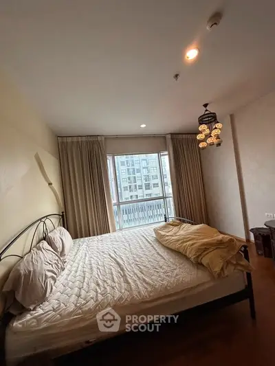 Cozy bedroom with large window and city view, featuring elegant lighting and neutral decor.