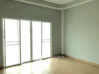 Spacious empty room with large sliding glass doors and wooden flooring, perfect for customization.