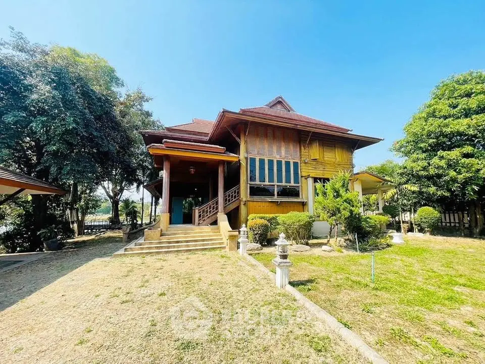 Charming traditional wooden house with lush garden and spacious yard under clear blue sky.