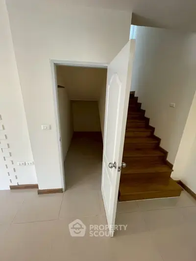 Modern interior with wooden staircase and open door leading to storage space, showcasing minimalist design.