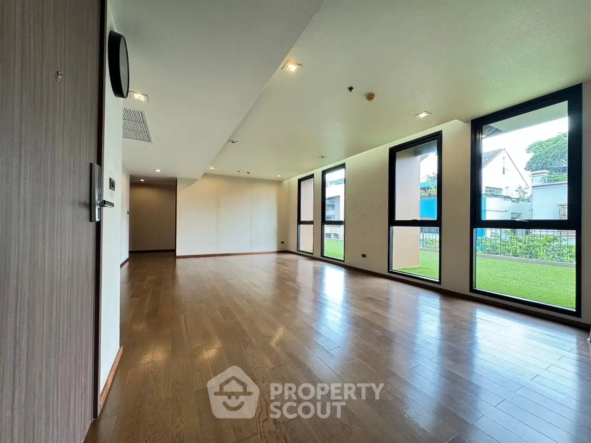 Spacious modern living room with large windows and wooden flooring, offering a bright and airy atmosphere.