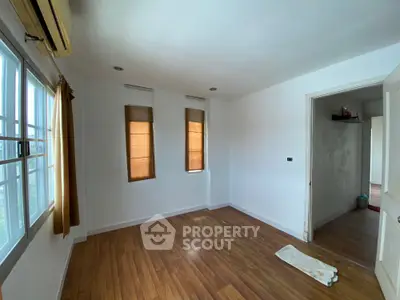 Spacious empty room with wooden flooring and large windows, perfect for customization.