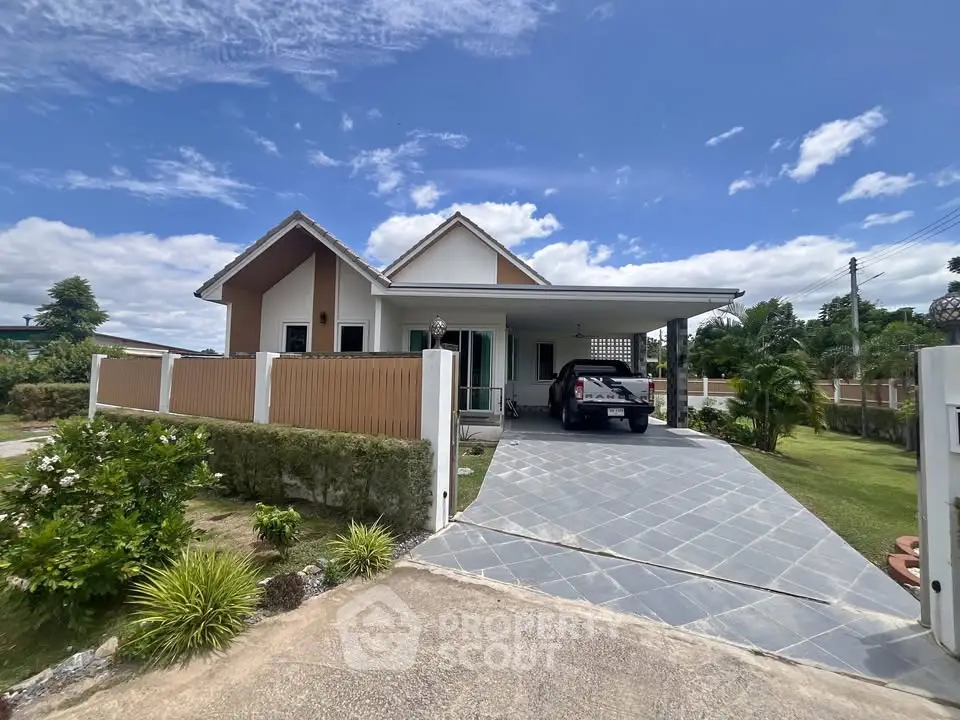 Charming single-story house with driveway and lush garden under a clear blue sky.