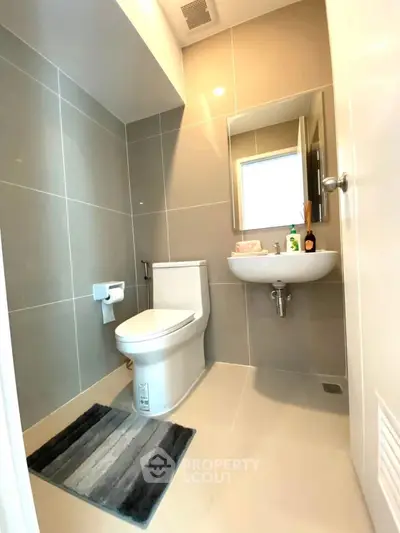 Modern bathroom with sleek design and neutral tones, featuring a toilet and wall-mounted sink.