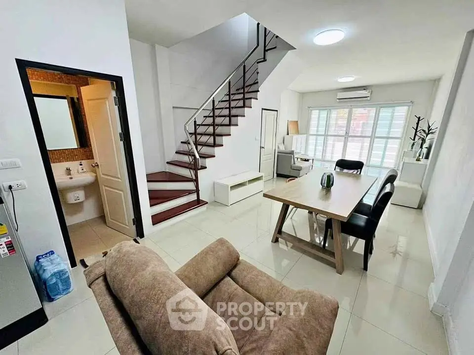 Modern living room with staircase, dining area, and natural light