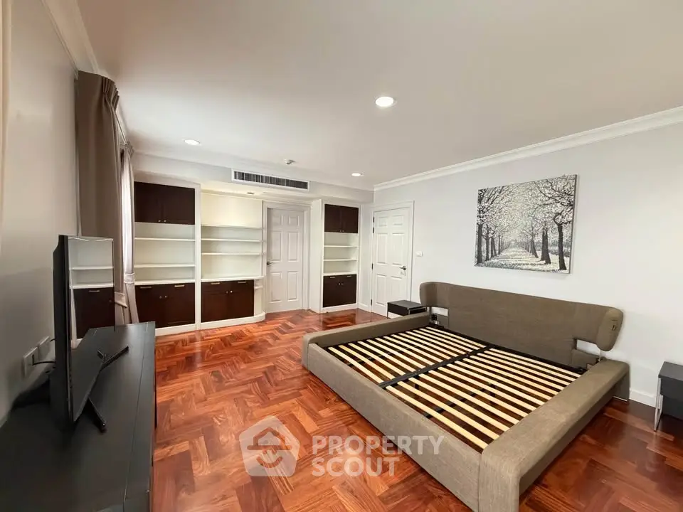 Spacious bedroom with elegant parquet flooring and built-in shelving, perfect for modern living.