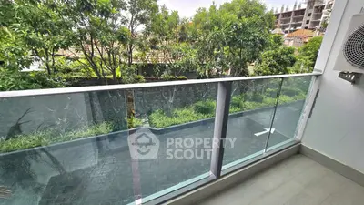 Modern balcony with glass railing and lush garden view in a serene residential setting.