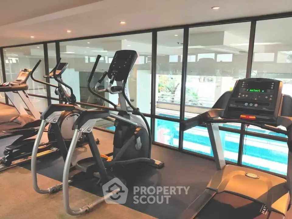 Modern gym with state-of-the-art equipment and pool view in luxury apartment complex.