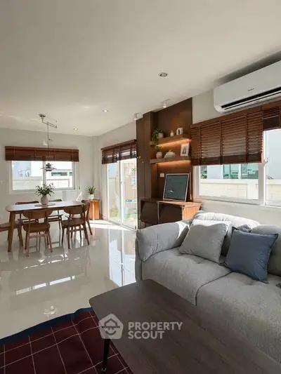 Spacious living room with modern decor and dining area, featuring large windows and natural light.