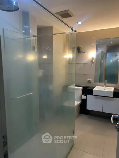 Modern bathroom with glass shower enclosure and sleek vanity in contemporary apartment.