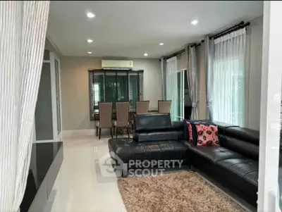 Spacious modern living room with elegant black leather sofa and dining area, perfect for entertaining.