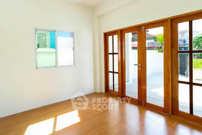 Bright and spacious room with wooden flooring and large glass doors leading to a sunny outdoor area.