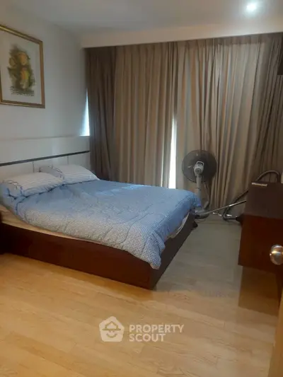 Cozy bedroom with wooden flooring and elegant curtains, featuring a comfortable bed and modern decor.