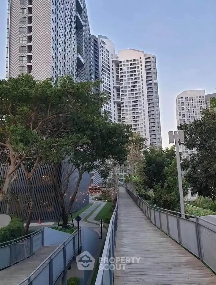 Modern high-rise residential buildings with lush greenery and a wooden walkway.