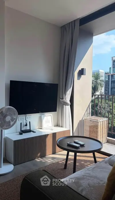 Modern living room with balcony view, featuring sleek TV setup and stylish decor in a contemporary apartment.