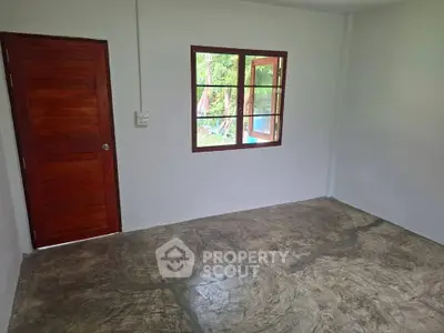 Minimalist empty room with wooden door and window, concrete floor, and garden view.